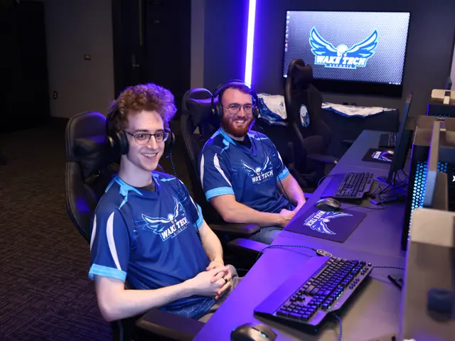 The image shows two men sitting at a desk in front of a computer, wearing headsets and smiling. On...