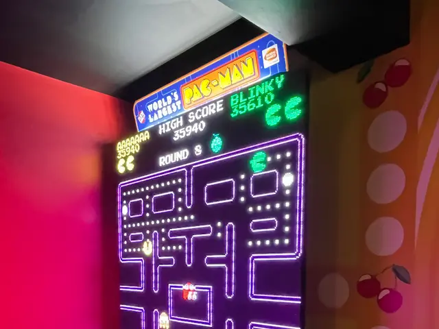The image shows a small arcade machine with a neon sign on top of it, featuring a colorful board...