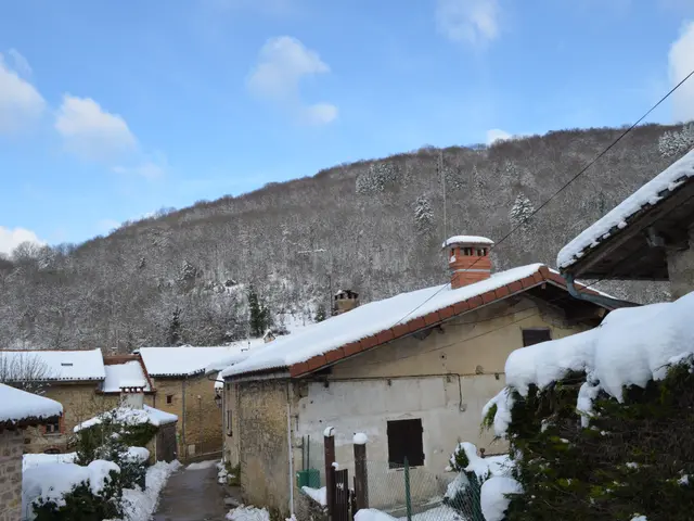 The image shows a picturesque winter scene of a small village nestled in the mountains, with...