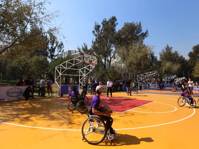 The image shows a group of people in wheelchairs playing basketball on a court surrounded by trees,...