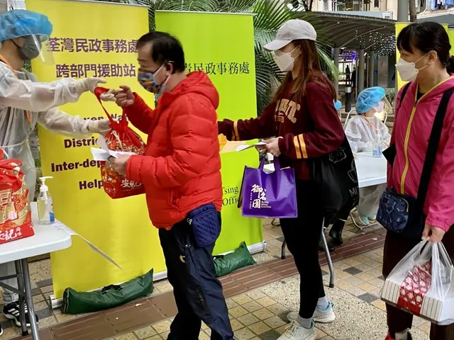 The image shows a group of people standing around a table with bags of food, wearing masks and...