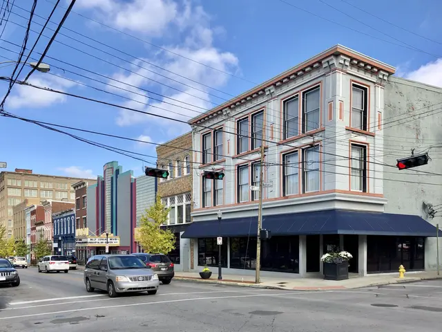 The image shows a city street with cars parked on the side of it, electric poles with wires,...