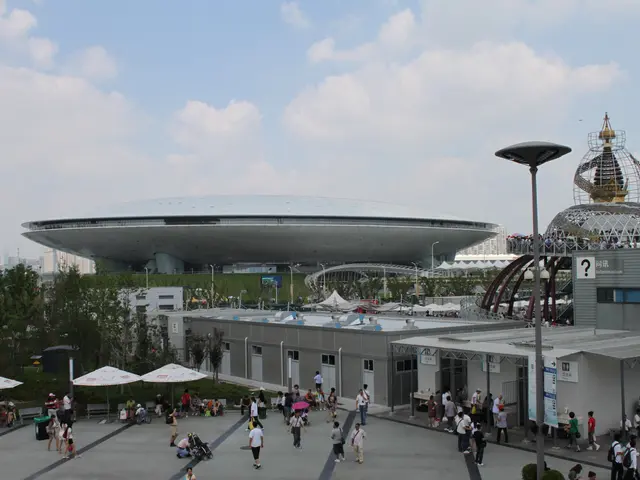 The image shows a group of people walking around in front of a large building, which is the Olympic...