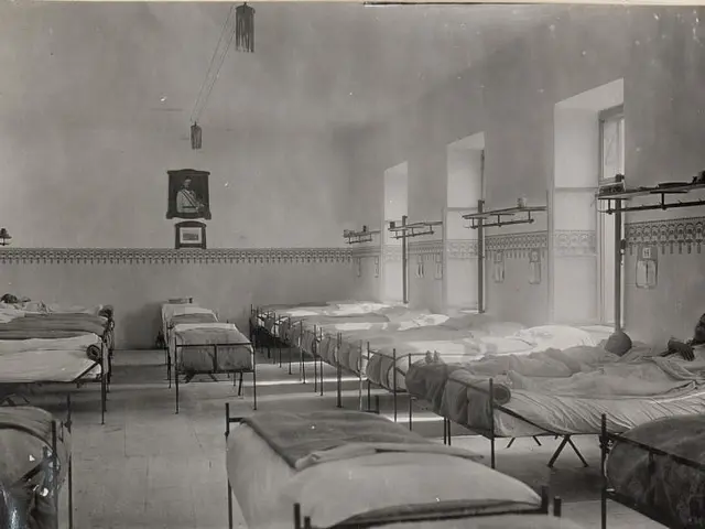 The image shows a black and white photo of a room filled with lots of beds, with a person lying on...
