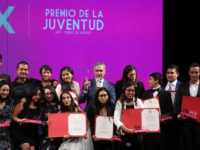The image shows a group of people standing on top of a stage, smiling and holding certificates in...