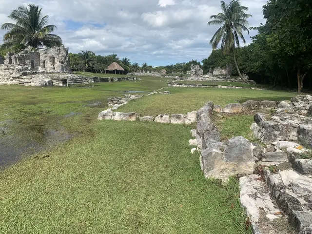 The image shows the ruins of the Mayan city of Tulum, Mexico, with lush green grass, rocks, and...
