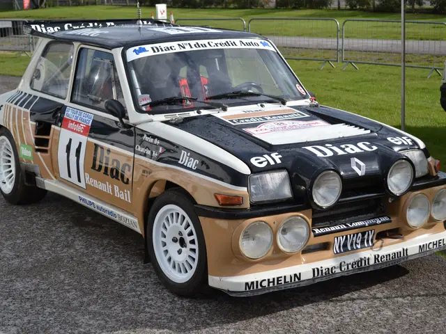 The image shows a Renault 5 Turbo RS Rally Car on the road surrounded by grass, railings, poles,...