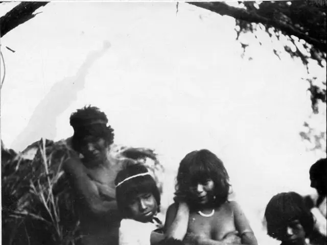 The image shows a black and white photo of a group of people standing next to each other in front...