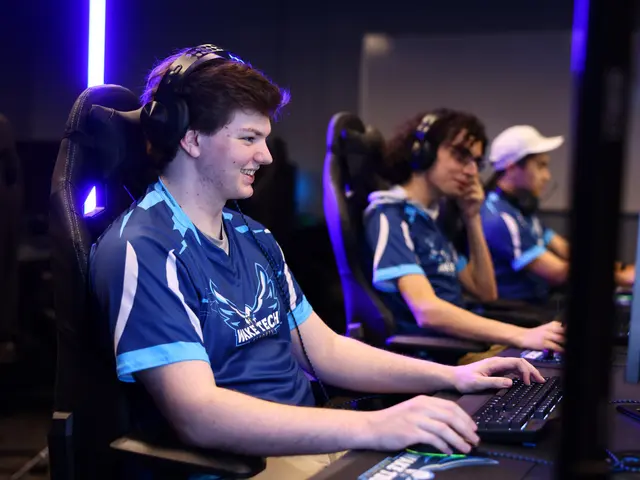 The image shows a group of young men sitting at a desk in front of a computer, wearing headsets and...