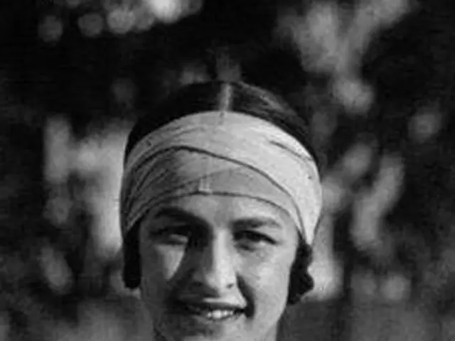 The image shows a black and white photo of a woman with a turban on her head, smiling, with a...